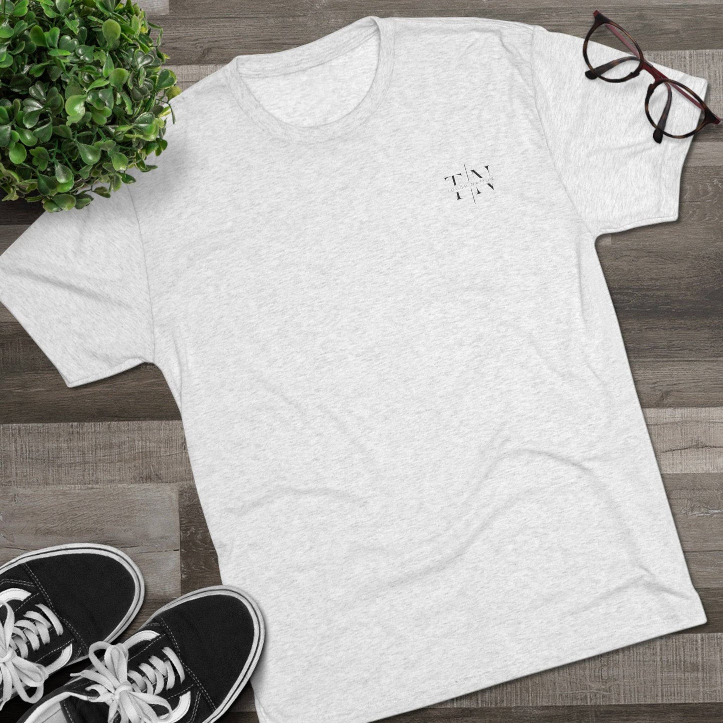 A lifestyle image showcasing a heather white Christian fitness shirt (left side logo) alongside athletic shoes, leaves, and glasses, perfect for an active lifestyle.