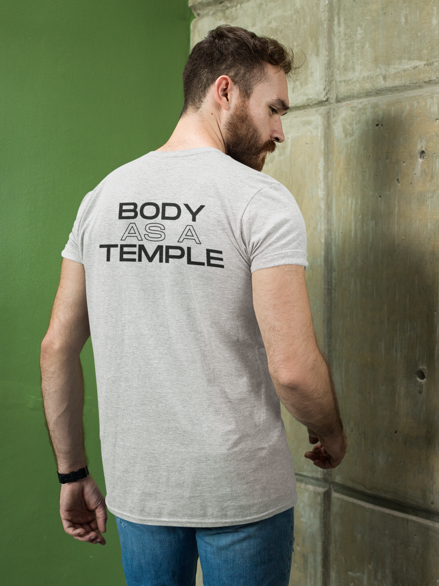 A Christian man confidently wearing a heather white shirt with the message 'Body As A Temple' on the back. His hands are in his pockets, conveying a sense of determination for Christ-centered fitness.